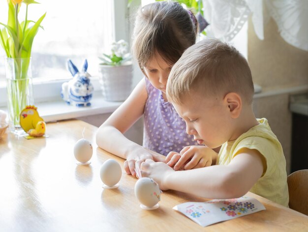Photo petite fille et garçon décorent des œufs de pâques à la maison se préparant pour le concept de pâque focus sélectif