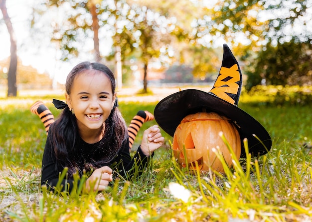 Petite fille et garçon découpant la citrouille à l'Halloween. Des enfants déguisés trompent ou traitent. Des bonbons ou un sort pour les enfants. Enfant en costume de sorcière jouant dans le parc en automne. Enfant en bas âge avec jack-o-lanterne.