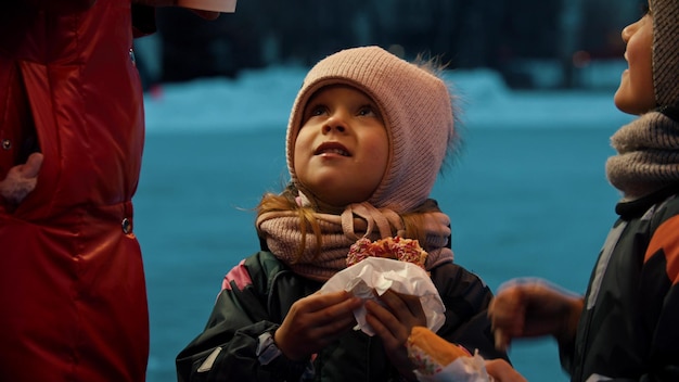 Une petite fille et un garçon mangeant des beignets à l'extérieur la fille regardant sa mère