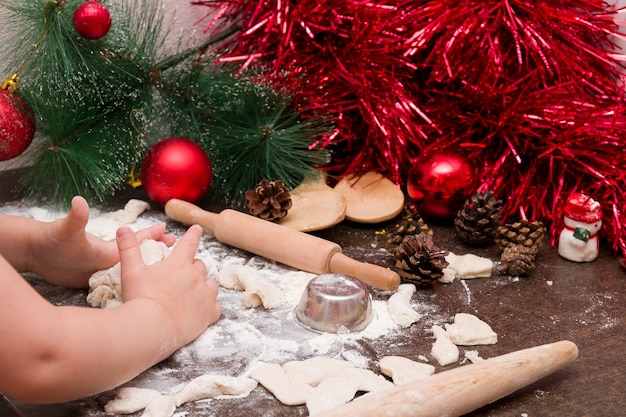 Petite fille, un garçon pétrit la pâte pour les biscuits de Noël contre des décorations de Noël lumineuses et des ustensiles de cuisine