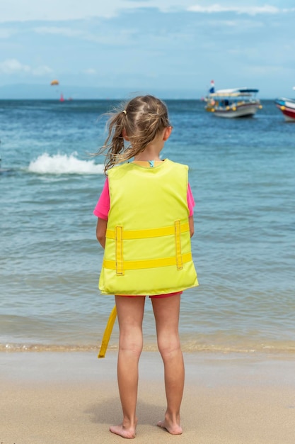 Petite fille en gilet de sécurité jaune debout devant l'océan