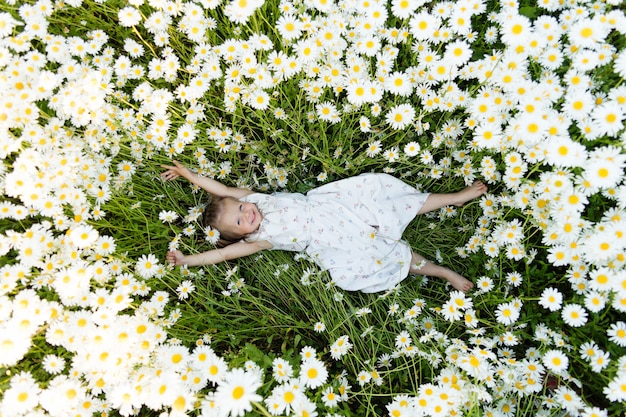 Petite fille gisant sur le sol dans les fleurs de marguerites