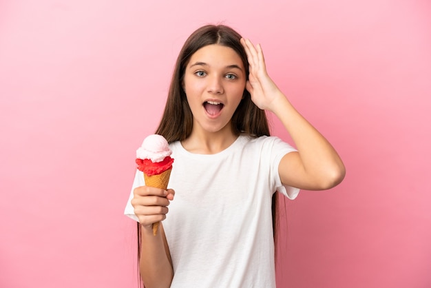 Petite fille avec une glace au cornet sur fond rose isolé avec une expression surprise