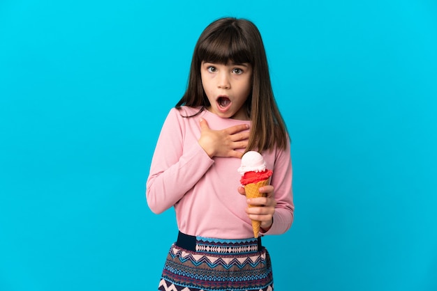 Petite fille avec une glace au cornet isolée sur fond bleu surprise et choquée en regardant à droite