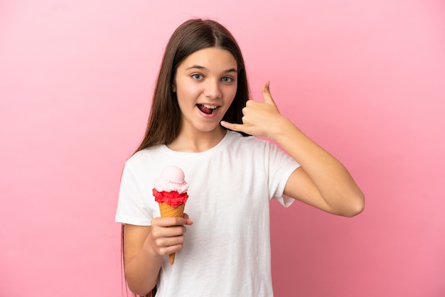 Petite fille avec une glace au cornet sur un mur rose isolé faisant un geste de téléphone