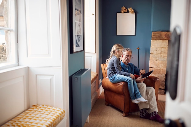 Photo petite-fille avec grand-père dans le fauteuil à la recherche de tablette numérique à la maison ensemble