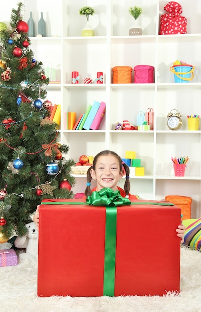 Petite fille avec une grande boîte-cadeau près de l'arbre de Noël