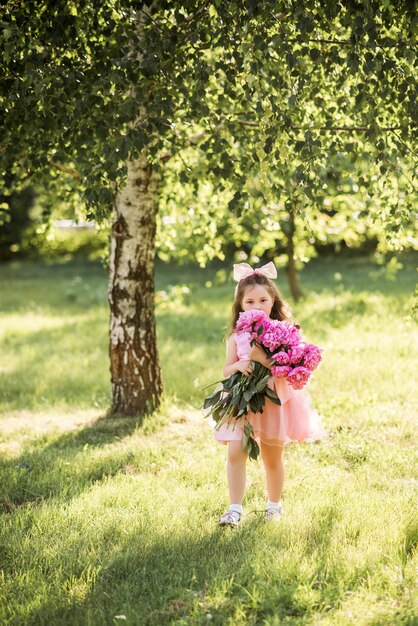 Petite fille avec un gros bouquet de pivoines. Un enfant se promène dans le parc fleuri en été.