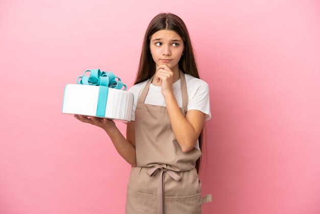 Petite fille avec un gros gâteau sur fond rose isolé ayant des doutes et pensant