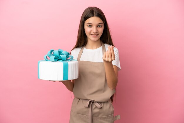 Petite fille avec un gros gâteau sur fond rose isolé faisant un geste d'argent