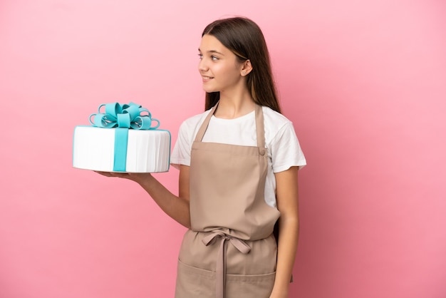 Petite fille avec un gros gâteau sur fond rose isolé regardant sur le côté