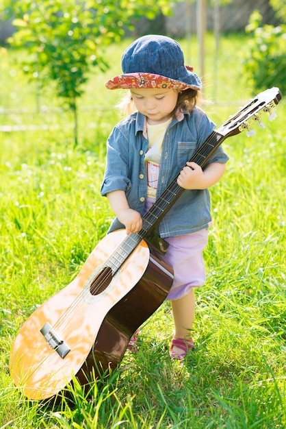 Une petite fille avec une grosse guitare acoustique s'amuse sur une pelouse verte