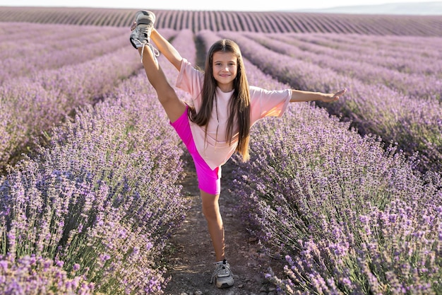 Petite fille gymnaste fait des exercices dans un champ de lavande au coucher du soleil