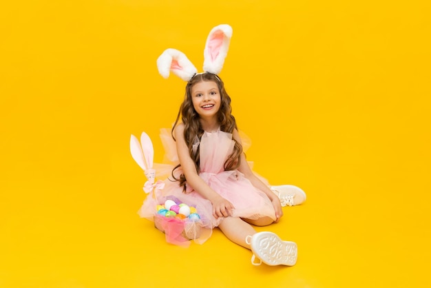 Une petite fille habillée comme un lapin de Pâques avec un panier d'œufs colorés sur un fond isolé jaune printemps festif Pâques