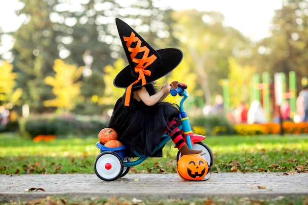 Petite fille habillée en costume de sorcière à vélo avec des citrouilles et des bonbons