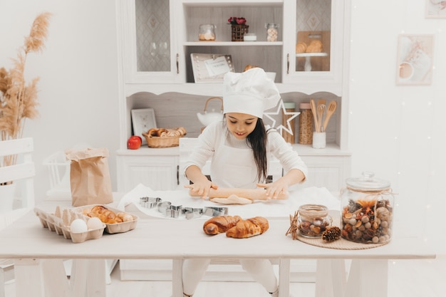 Une petite fille habillée en cuisinière dans la cuisine prépare des cookies.