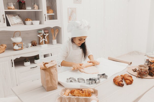 Une petite fille habillée en cuisinière dans la cuisine prépare des cookies.