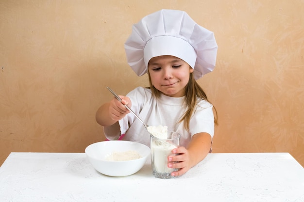 Une petite fille habillée en cuisinière pétrit la pâte Concept de mode de vie de l'enfant de cuisine L'enfant aime s'amuser en étudiant et en jouant dans la cuisine