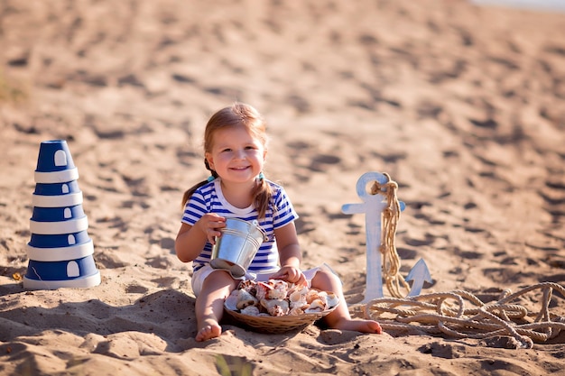 Petite fille habillée en marin sur une plage de sable avec des coquillages au bord de la mer