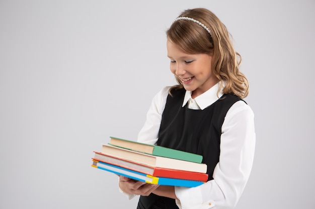 Petite fille habillée pour l'école tenant une pile de livres