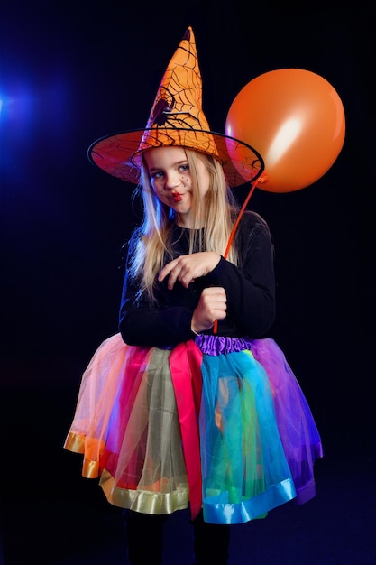 Une petite fille habillée en sorcière avec une citrouille sur un fond sombre à la lumière de projecteurs multicolores