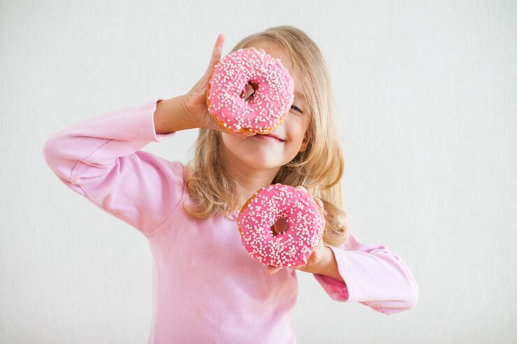Petite fille heureuse aux cheveux blonds jouant et dégustation de beignets avec glaçage rose à la célébration de Hanoucca