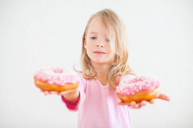 Petite Fille Heureuse Aux Cheveux Blonds Jouant Et Dégustation De Beignets Avec Glaçage Rose à La Célébration De Hanoucca