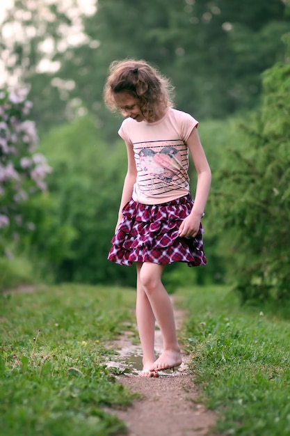 Une petite fille heureuse aux pieds nus marche dans des flaques d'eau après la pluie d'été à la campagne.