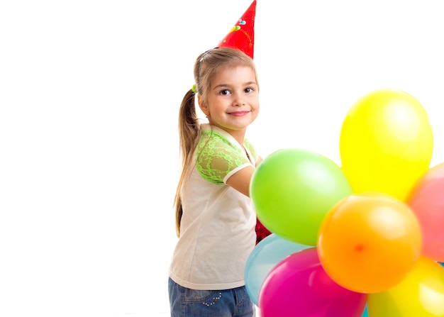 Petite fille heureuse célébrant l'anniversaire avec des ballons multicolores dans un chapeau rouge de fête