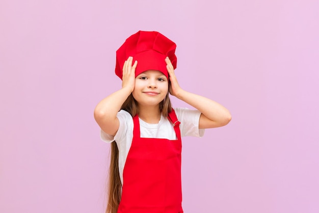 Une petite fille heureuse en costume de chef est très heureuse et souriante la fille aime beaucoup aider les professeurs en cuisine