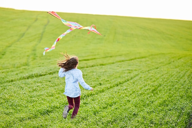 Petite fille heureuse courir avec kate dans les mains sur le champ de blé vert Grand cerf-volant arc-en-ciel coloré avec longue queue