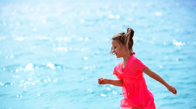 La petite fille heureuse court sur la plage en été