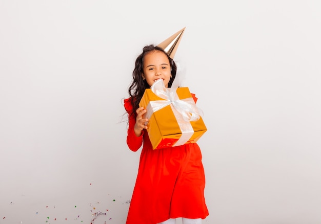 Une petite fille heureuse dans une casquette d'anniversaire tient une grande boîte-cadeau rouge. concept de vacances, place pour le texte