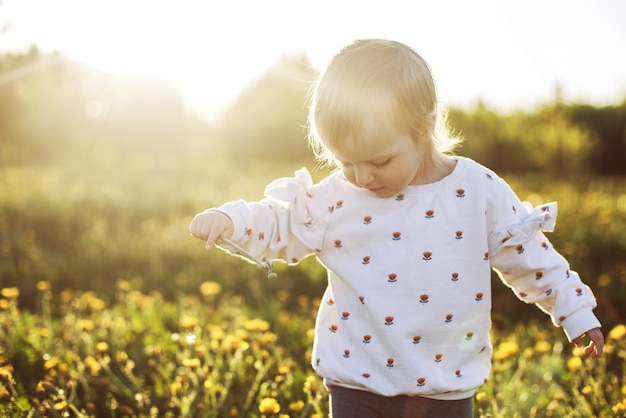 petite fille heureuse dans un champ avec un pissenlit à la main