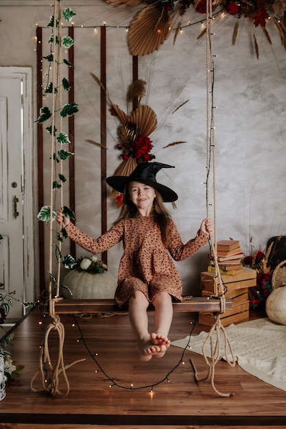 Une petite fille heureuse dans un chapeau de sorcière est assise sur une balançoire et se balance