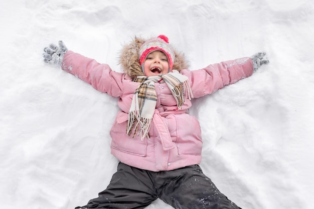 Petite fille heureuse dans des vêtements chauds se trouve sur la neige