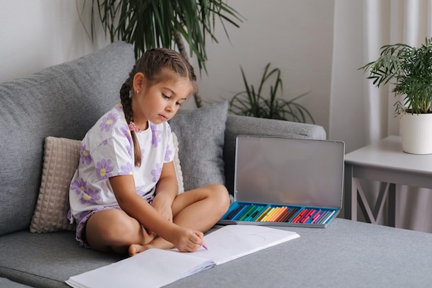 Une petite fille heureuse dessine dans un album à la maison. Une fille de cinq ans dessine après la maternelle.