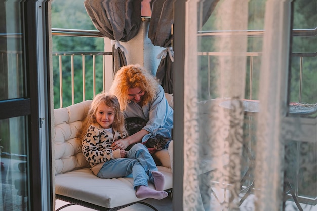 Une petite fille heureuse un enfant avec un sourire joue sur une vernada de printemps d'été à la maison avec maman et un chat