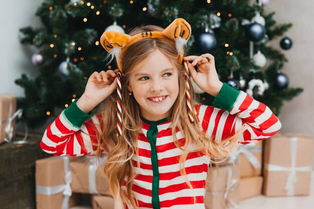 Une petite fille heureuse est assise avec des bonbons près de l'arbre de Noël. Noël.