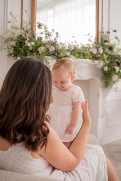 Une petite fille heureuse est assise dans les bras d'une mère brune sur une chaise dans la chambre