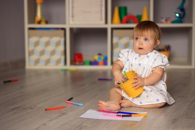 petite fille heureuse est assise sur le sol et dessine sur papier avec des crayons de couleur