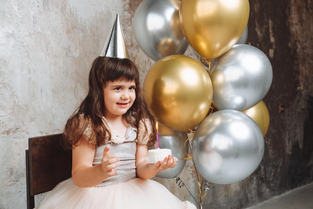 Une petite fille heureuse fait un vœu et souffle les bougies sur les ballons de gâteau Espace pour texte mur décoratif anniversaire