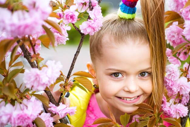 Petite fille heureuse jouant sous un cerisier en fleurs avec des fleurs roses fille appréciant la fleur de cerisier