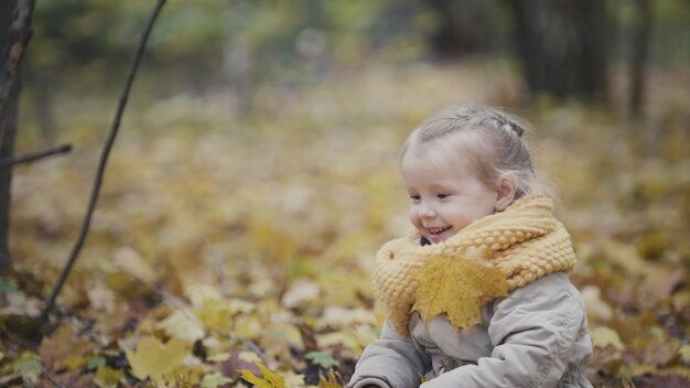 Petite fille heureuse joue dans le parc d'automne parmi les feuilles jaunes, téléobjectif