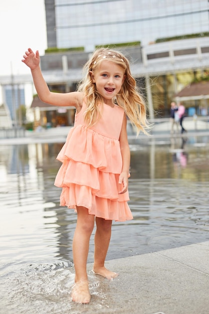 Une petite fille heureuse joue avec de l'eau dans une fontaine sur la place