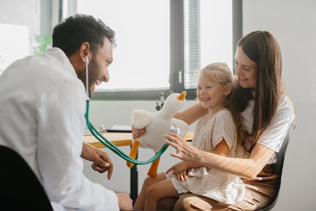 Photo une petite fille heureuse, une mère et un médecin de famille jouant à un jeu amusant avec un jouet et un stéthoscope.
