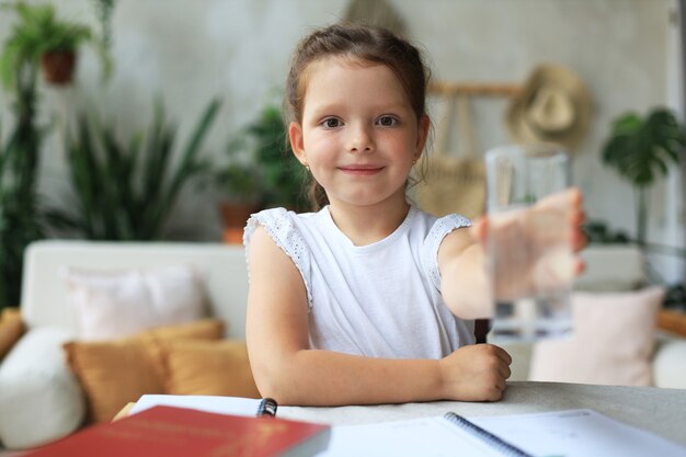 Une petite fille heureuse offre de l'eau minérale cristalline en verre, un petit enfant recommande une dose quotidienne d'eau propre.