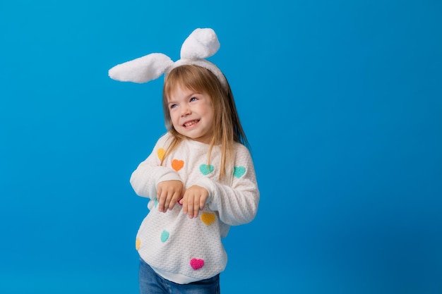 Une petite fille heureuse avec des oreilles de lapin sur la tête et une boîte-cadeau sur un fond bleu Espace concept de Pâques pour le texte