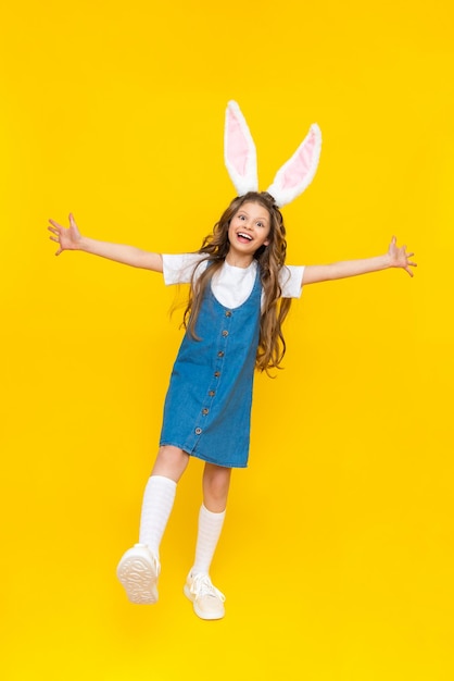 Une petite fille heureuse profite des vacances de printemps de Pâques pour les enfants Un enfant habillé comme un lapin avec de longues oreilles Une charmante dame aux cheveux bouclés sur fond jaune isolé