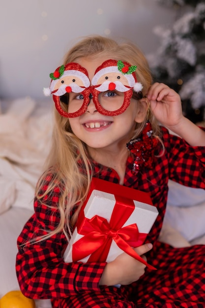 une petite fille heureuse en pyjama à la maison se réjouit et déballe des cadeaux pour Noël. Photo de haute qualité